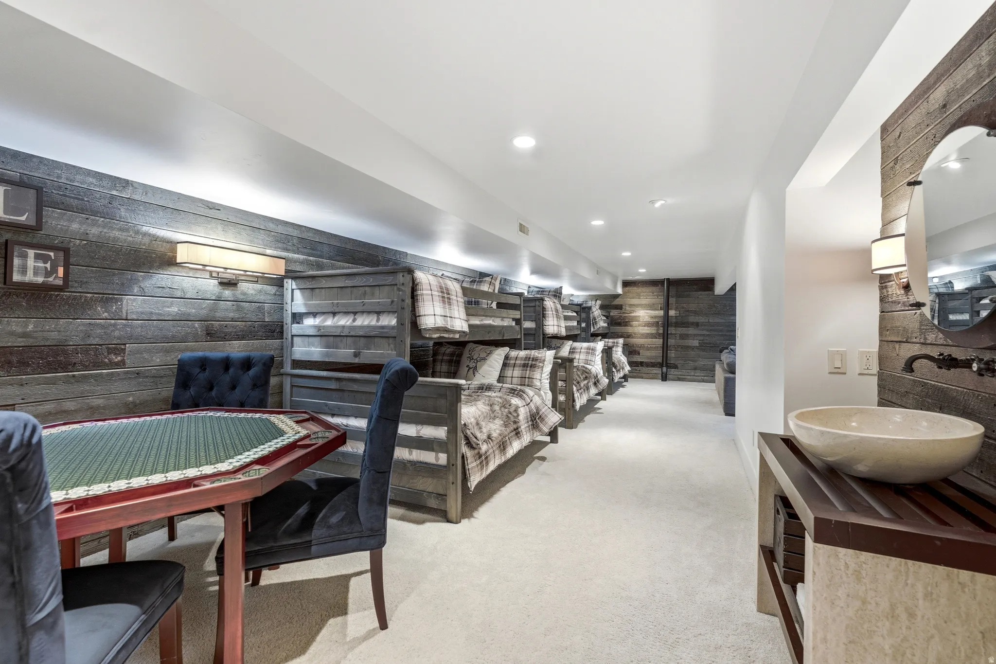 Carpeted lower-level space featuring rustic wood-finish accent walls, built-in bunk beds, recessed lighting, and a dedicated vanity area with a vessel sink