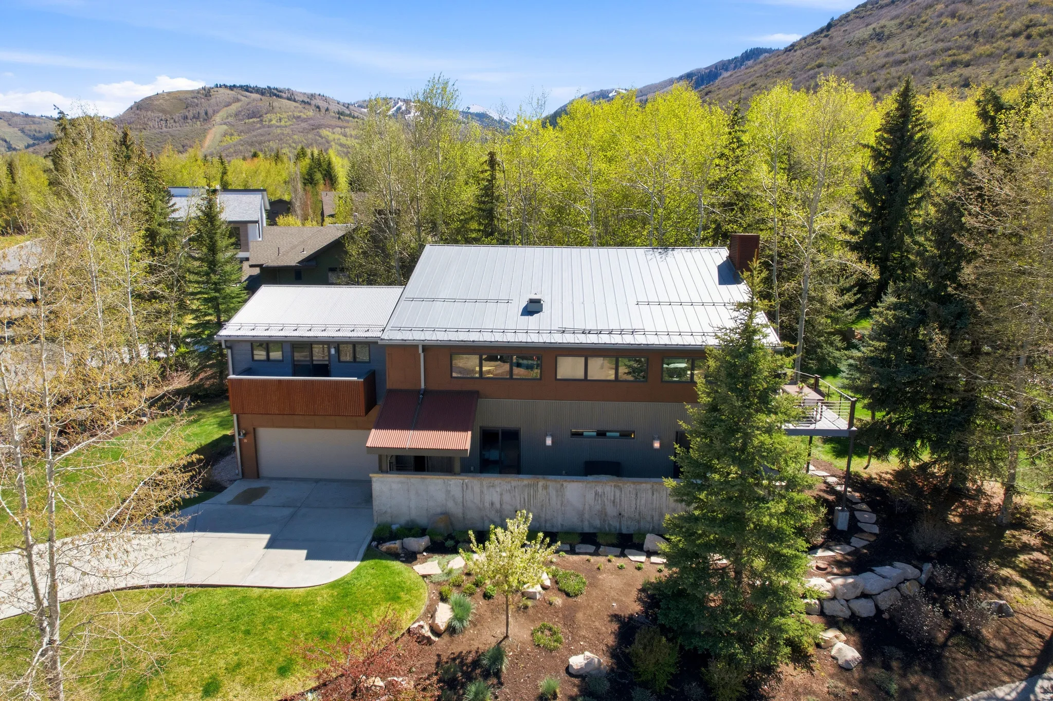 Modern multi-level residence featuring a metal roof, contrasting exterior panels, extensive window placements, and a concrete driveway