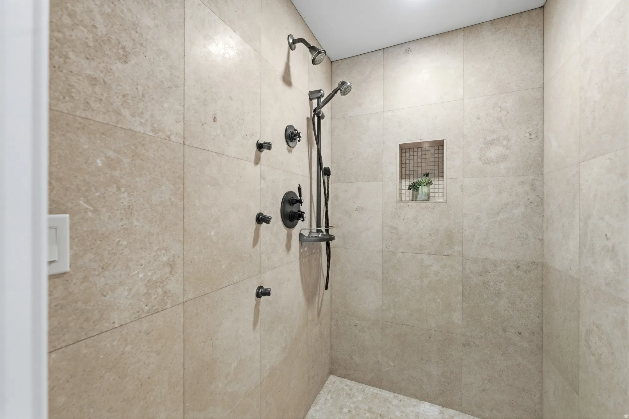 Walk-in shower featuring large format natural stone-look tile, a built-in niche with mosaic tile, a ceiling-mounted rain shower head, a handheld shower fixture, and multiple body jets with a matte black finish