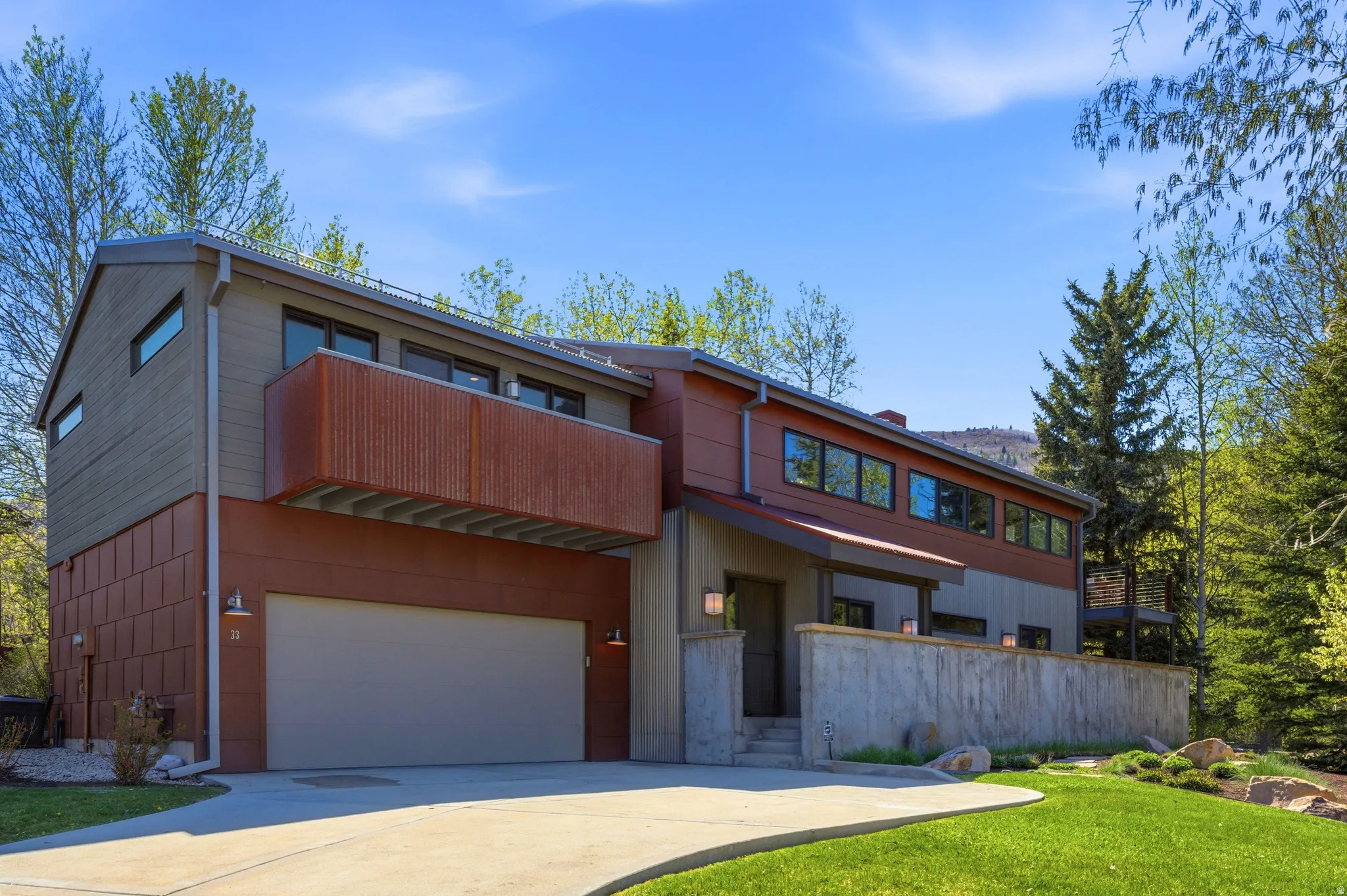 Contemporary exterior featuring mixed-material siding, an attached garage, a private balcony with metal screening, and multiple large windows