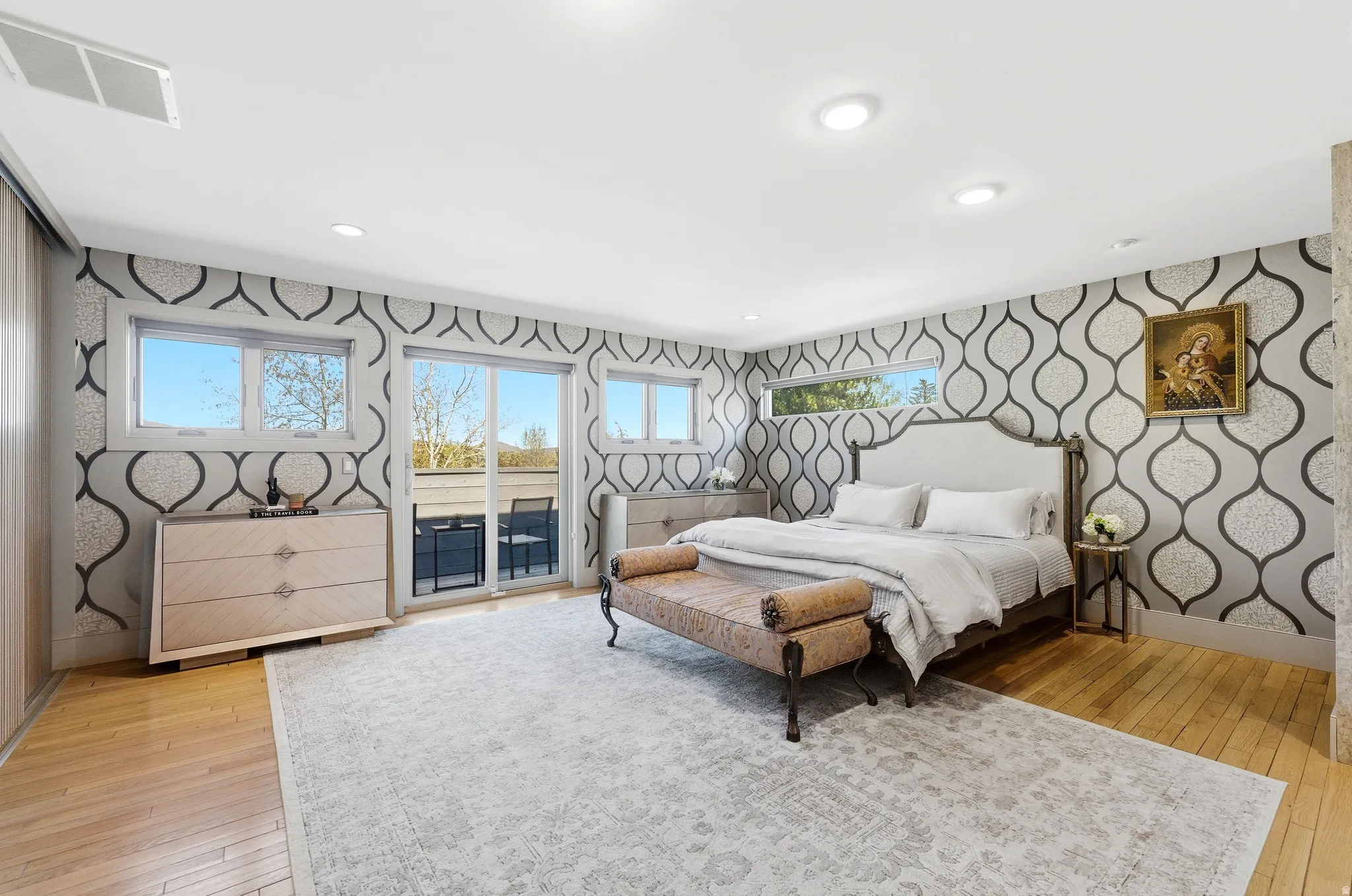 Bedroom with patterned accent walls, wood-finish flooring, recessed lighting, and a sliding glass door leading to an outdoor balcony