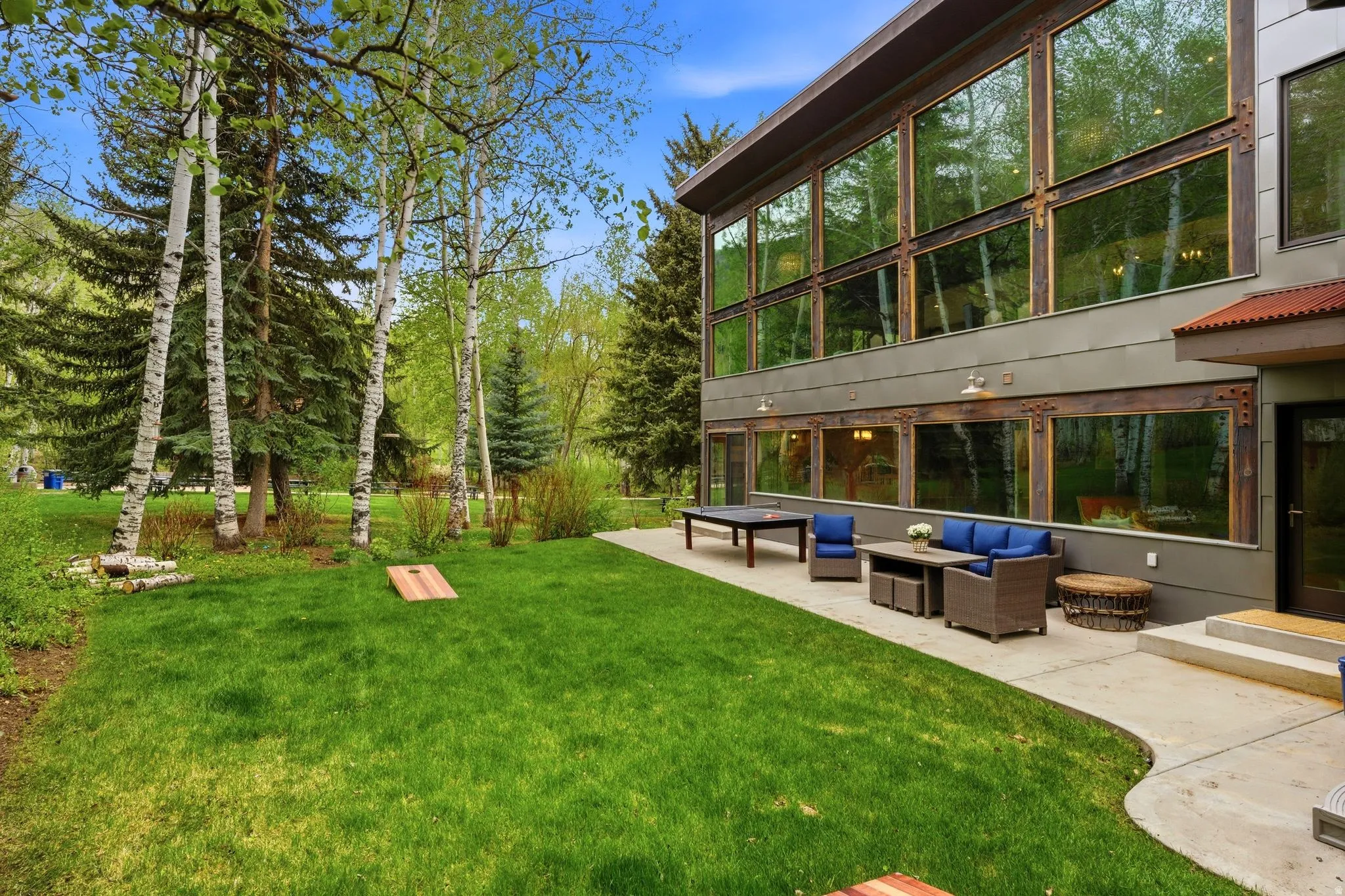 Contemporary exterior with expansive floor-to-ceiling windows, a large concrete patio, and a manicured lawn