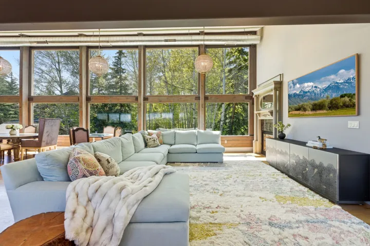 Floor-to-ceiling windows with wood framing, two woven pendant light fixtures, and a decorative fireplace surround with mantel