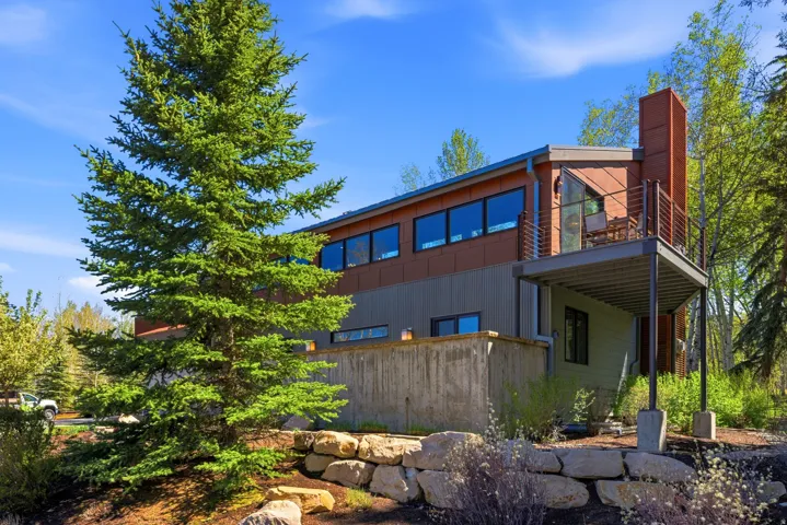 Contemporary architectural design featuring multi-toned horizontal siding, expansive upper-level windows, a cantilevered balcony with metal railing, and a prominent stone retaining wall