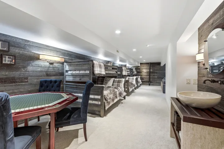 Carpeted lower-level space featuring rustic wood-finish accent walls, built-in bunk beds, recessed lighting, and a dedicated vanity area with a vessel sink
