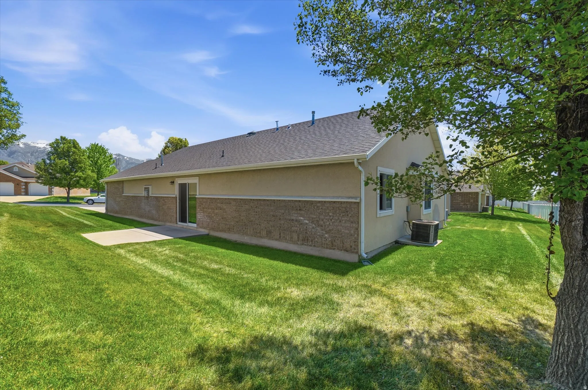 Spacious rear yard with a concrete patio, lush green lawn, and mature trees