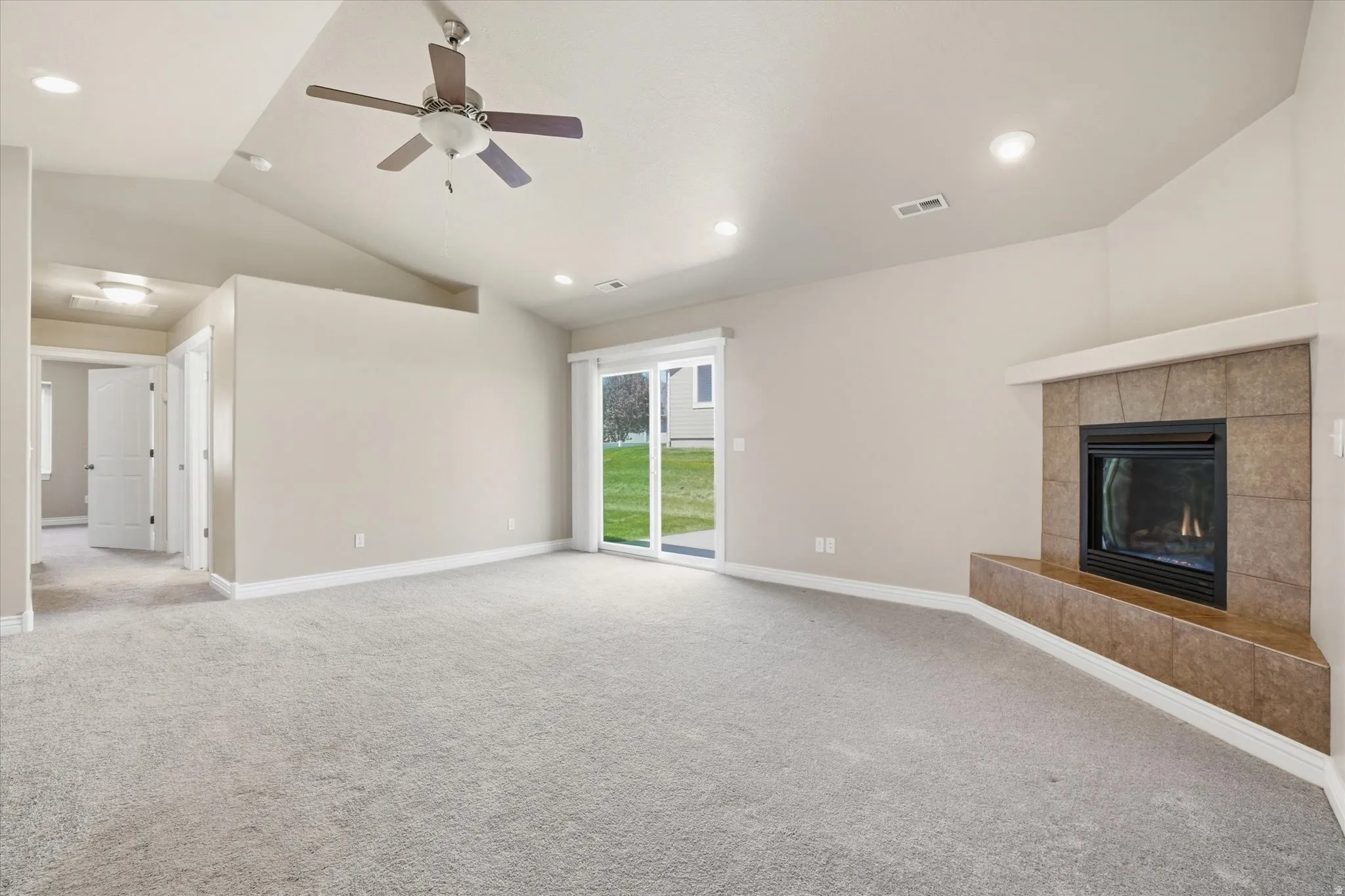 Spacious room featuring vaulted ceilings, a tiled fireplace with hearth, and plush carpeting