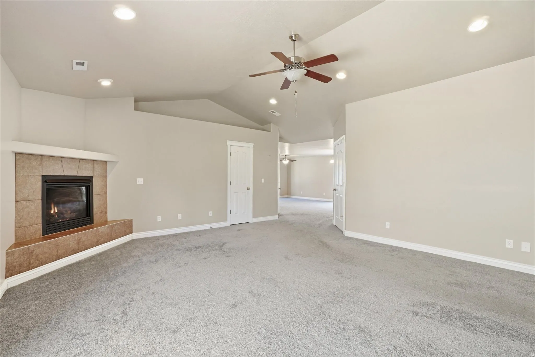 Spacious carpeted room featuring a corner fireplace with a tiled surround, a vaulted ceiling, recessed lighting, and a ceiling fan