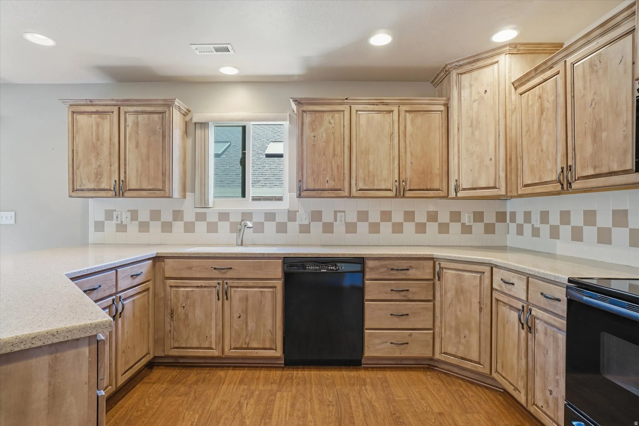 Kitchen featuring wood-finish cabinetry with dark hardware, a light-toned countertop, and a tiled backsplash