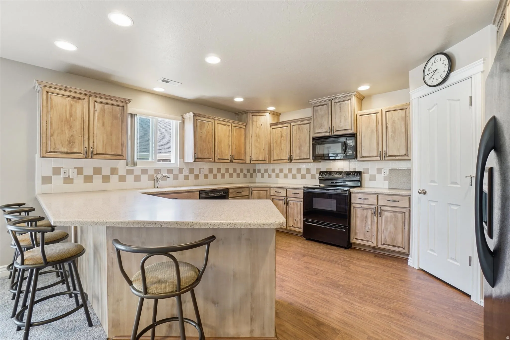 Kitchen featuring extensive light wood cabinetry, a checkered tile backsplash, black appliances, recessed lighting, and wood-finish flooring