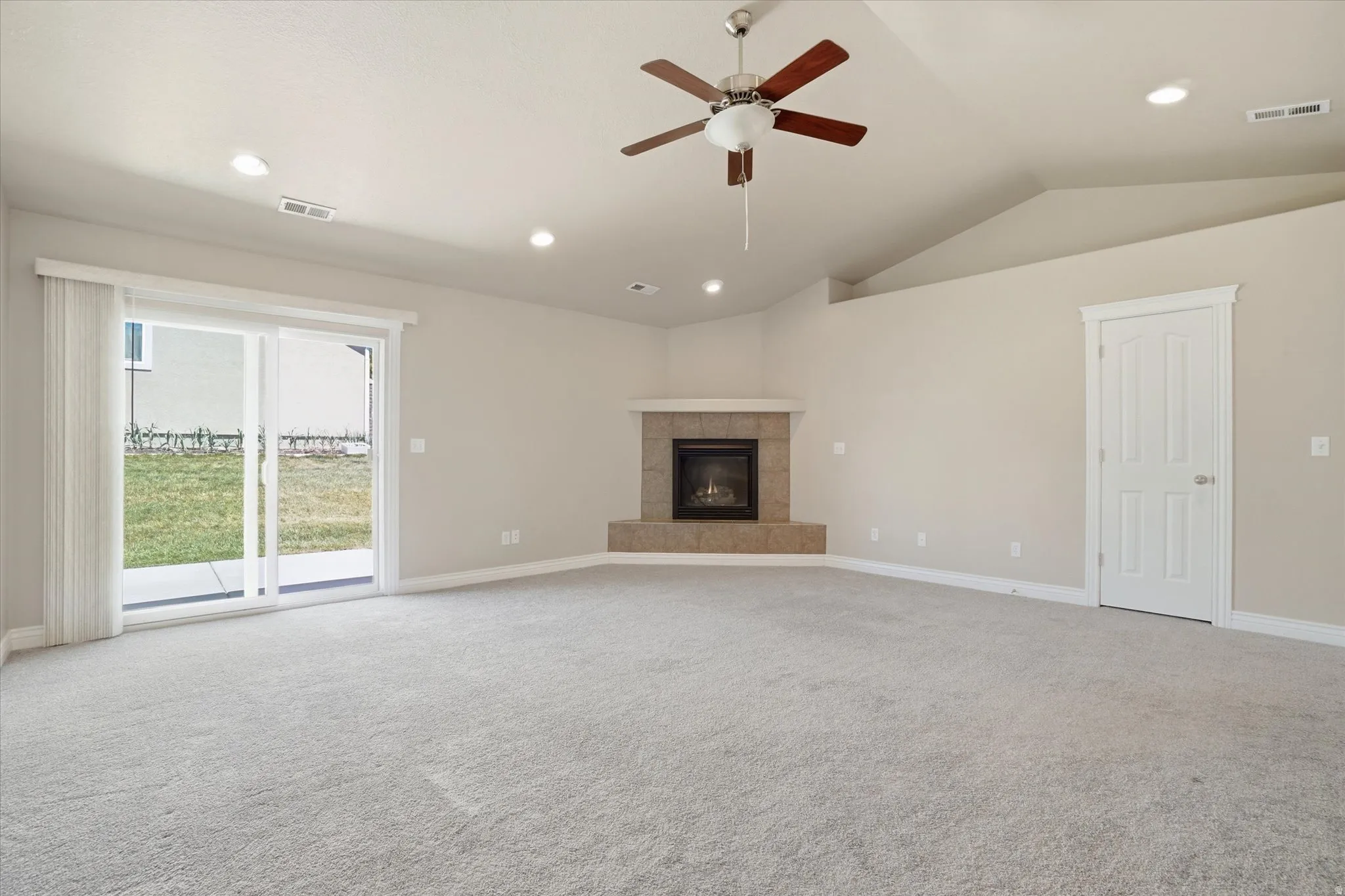 Spacious living area featuring a corner fireplace with a tiled surround, light-toned carpeting, and a ceiling fan