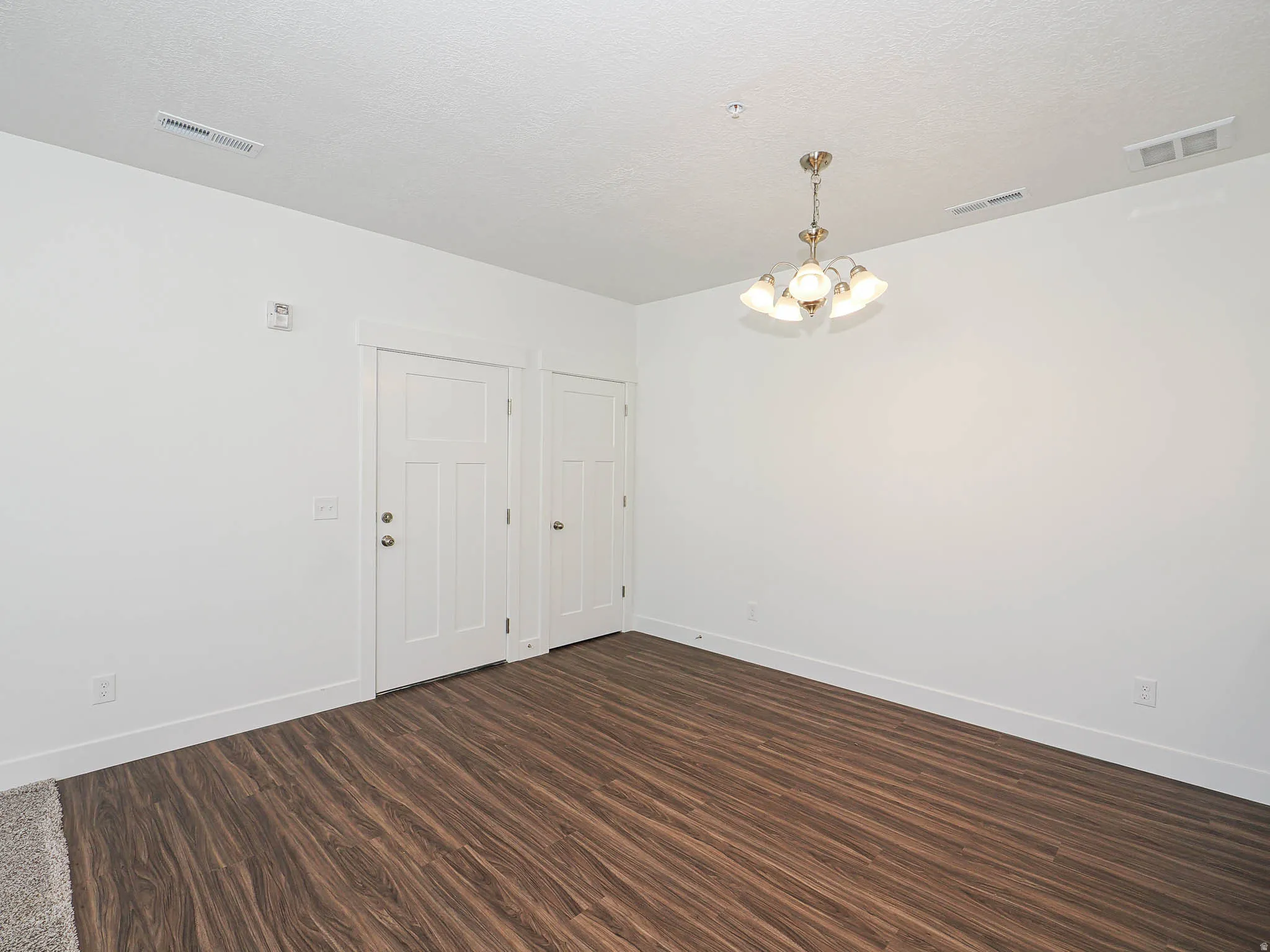 Spacious room featuring wood-finish flooring and a contemporary chandelier