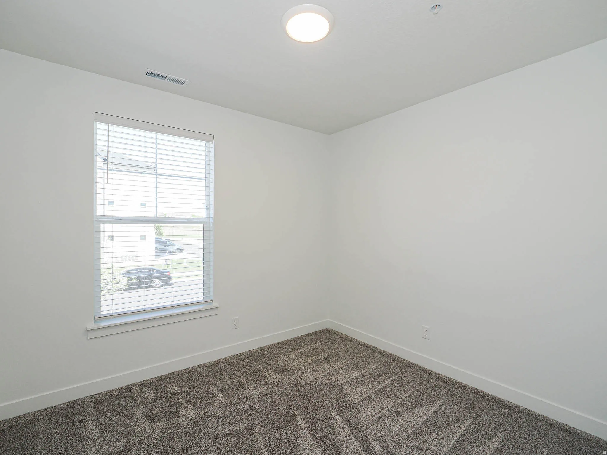 Bedroom featuring a window with blinds, recessed ceiling light, white walls, and patterned carpet flooring