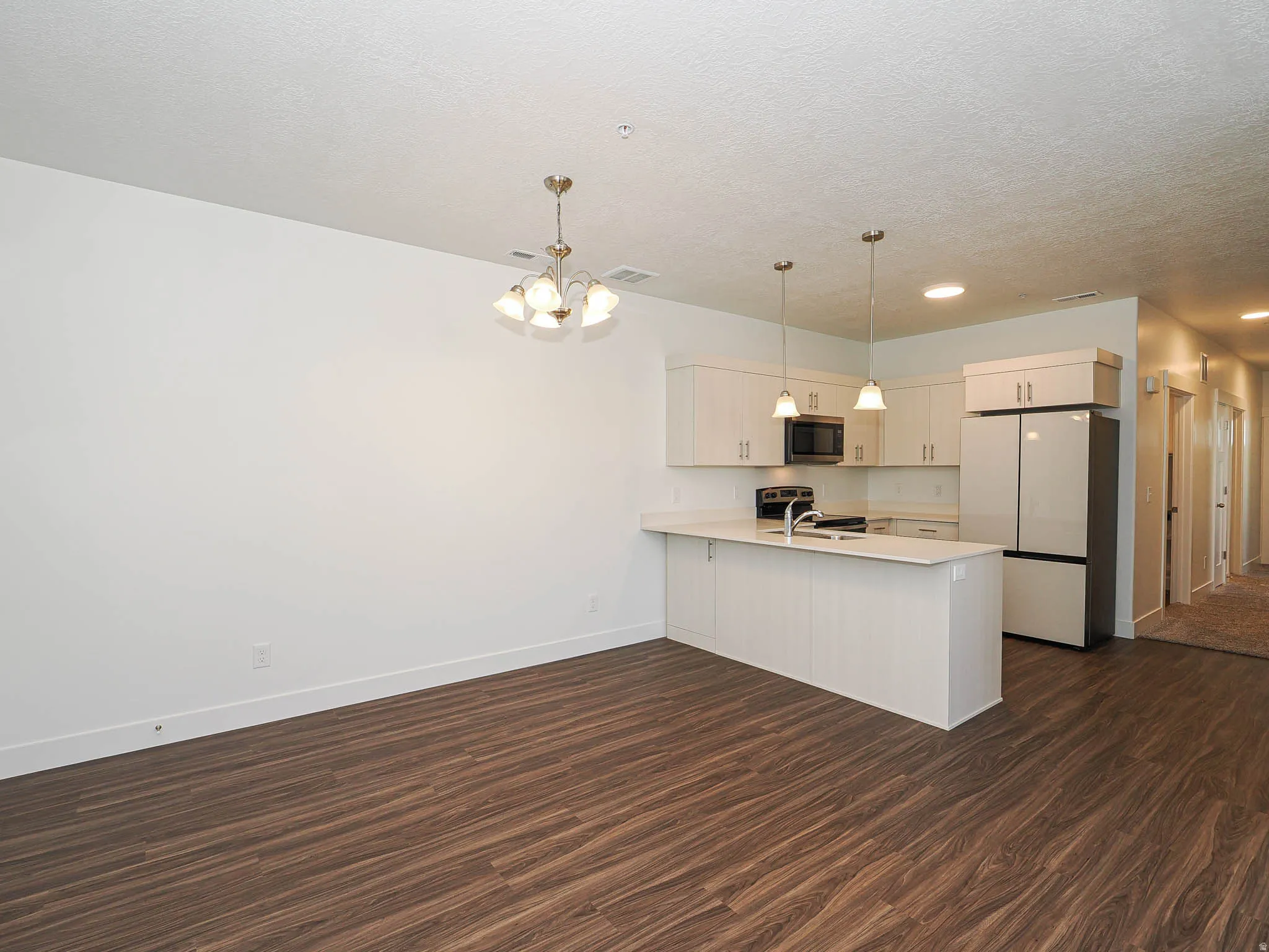 Kitchen featuring light-toned cabinetry, a large kitchen island with a sink, pendant lighting, stainless steel appliances, and wood-finish flooring