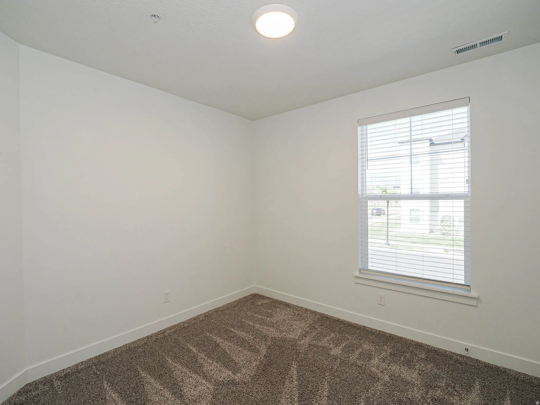 Room featuring neutral-toned walls, textured carpeting, and a window with blinds