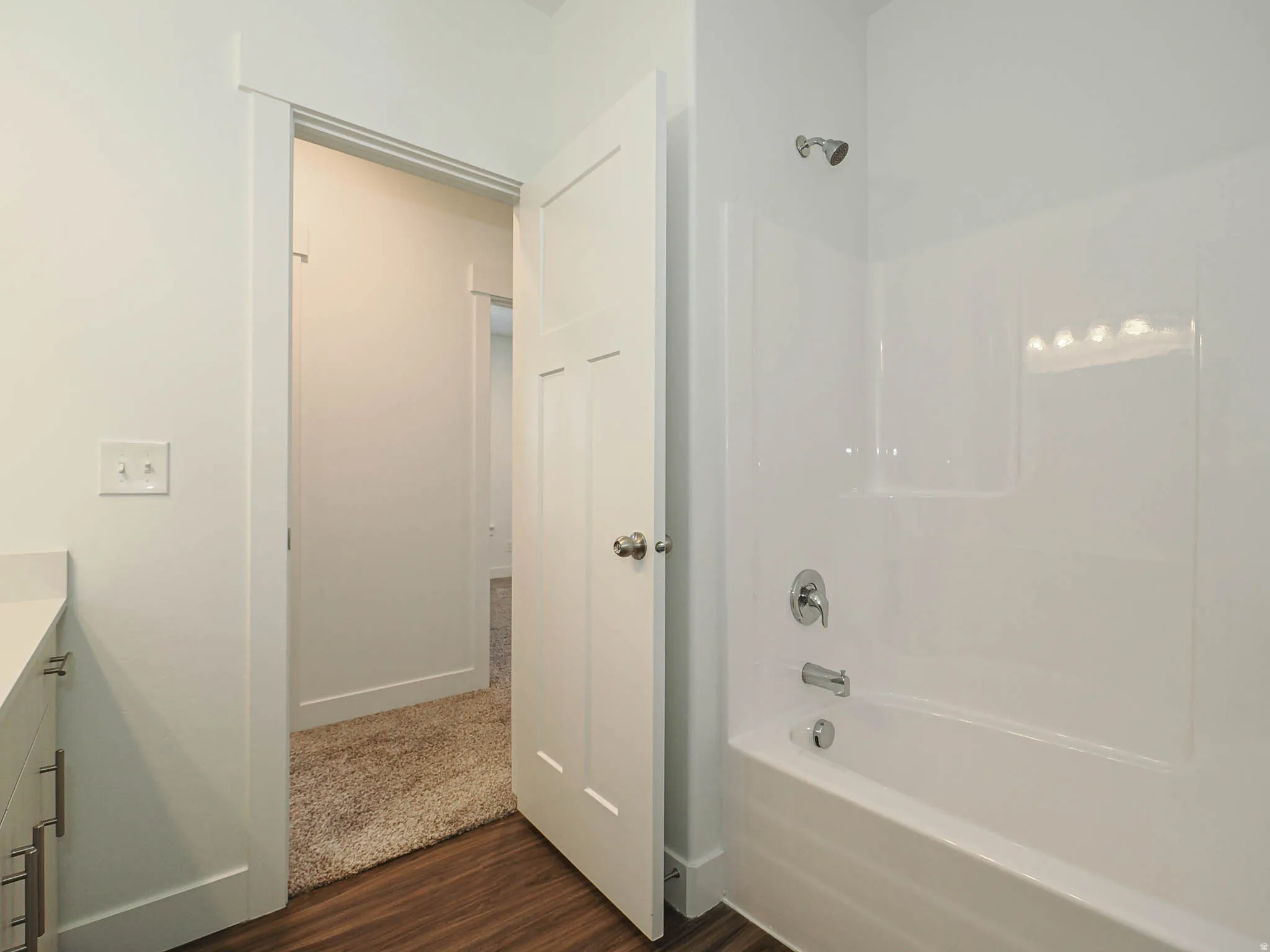 Bathroom featuring a white tub and shower surround, chrome shower fixtures, and dark wood-finish flooring