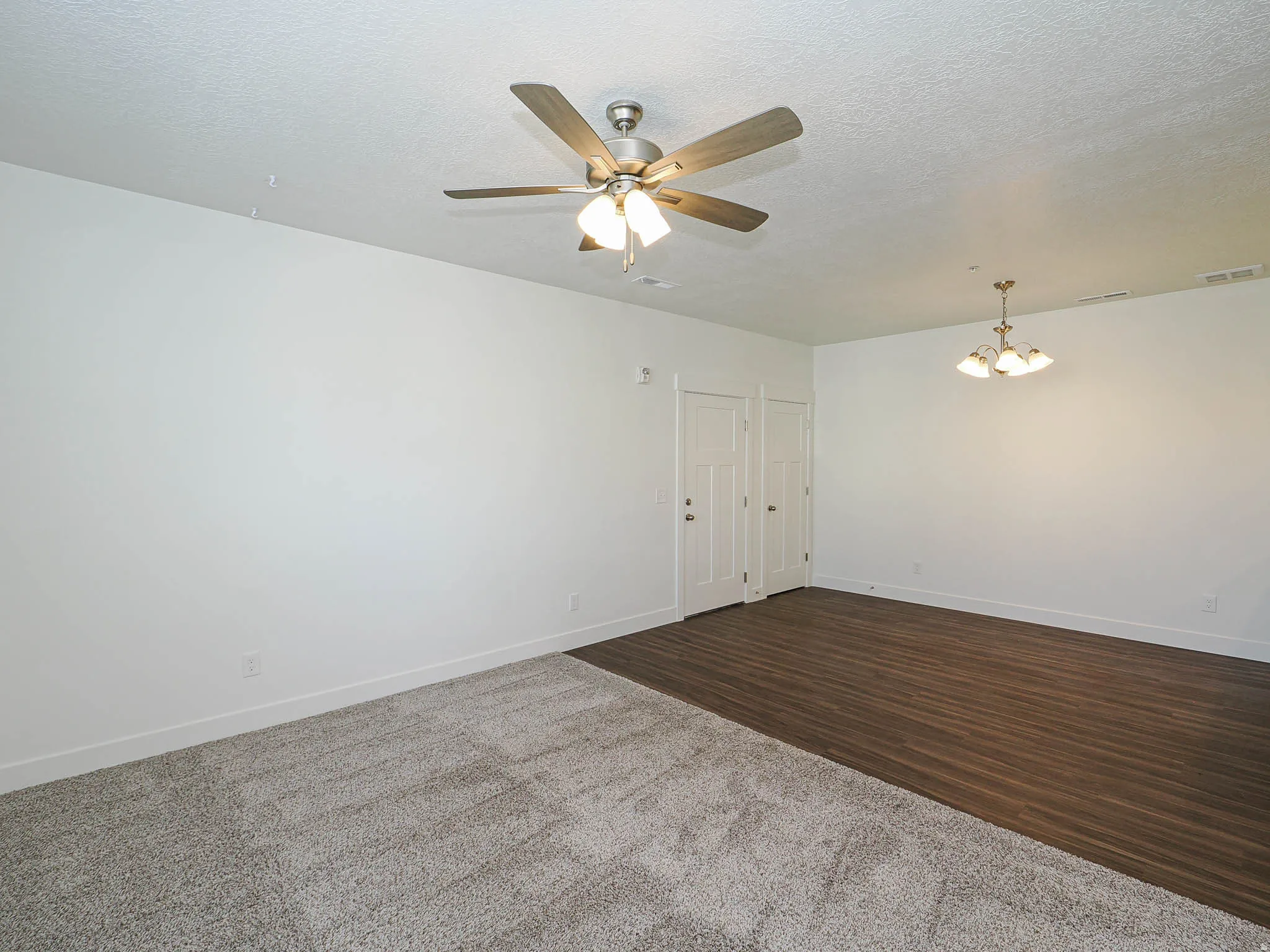 Interior space featuring a ceiling fan, dual white panel doors, wood-finish flooring, and light-toned carpeting
