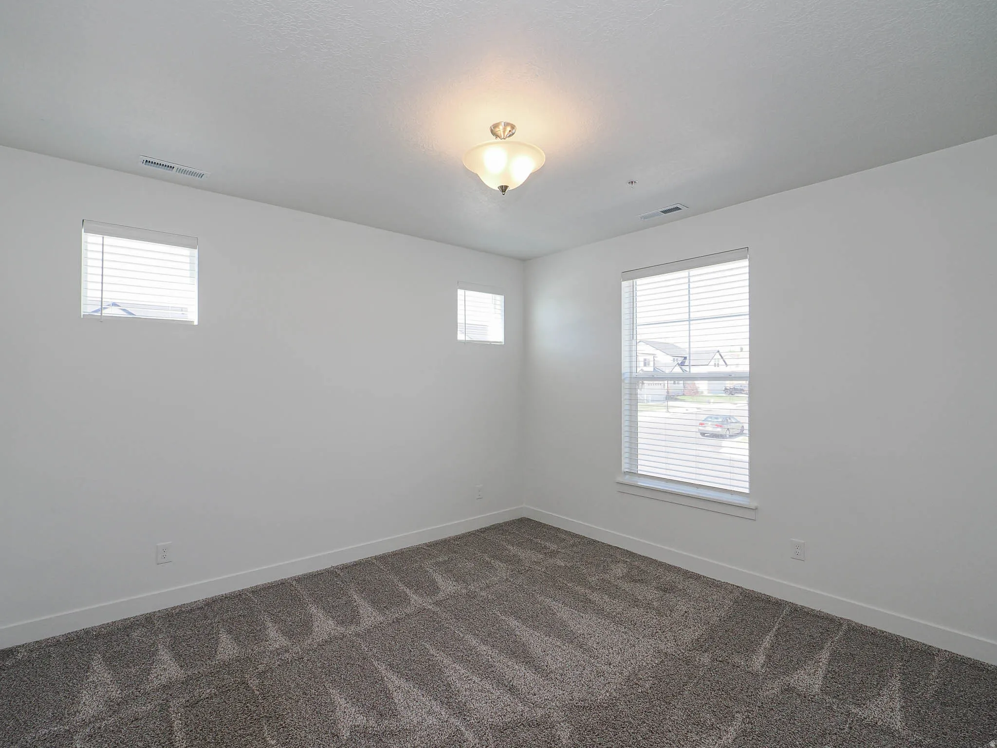 Spacious interior featuring neutral wall paint, gray patterned carpeting, and three windows with white blinds