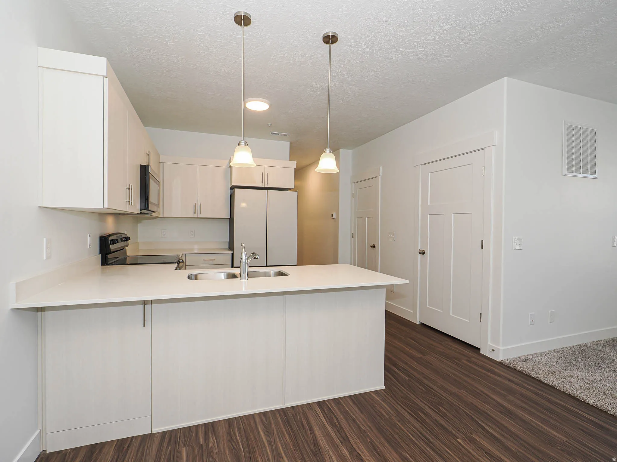 Modern kitchen featuring white cabinetry, light countertops, wood-finish flooring, and two pendant lights over the island