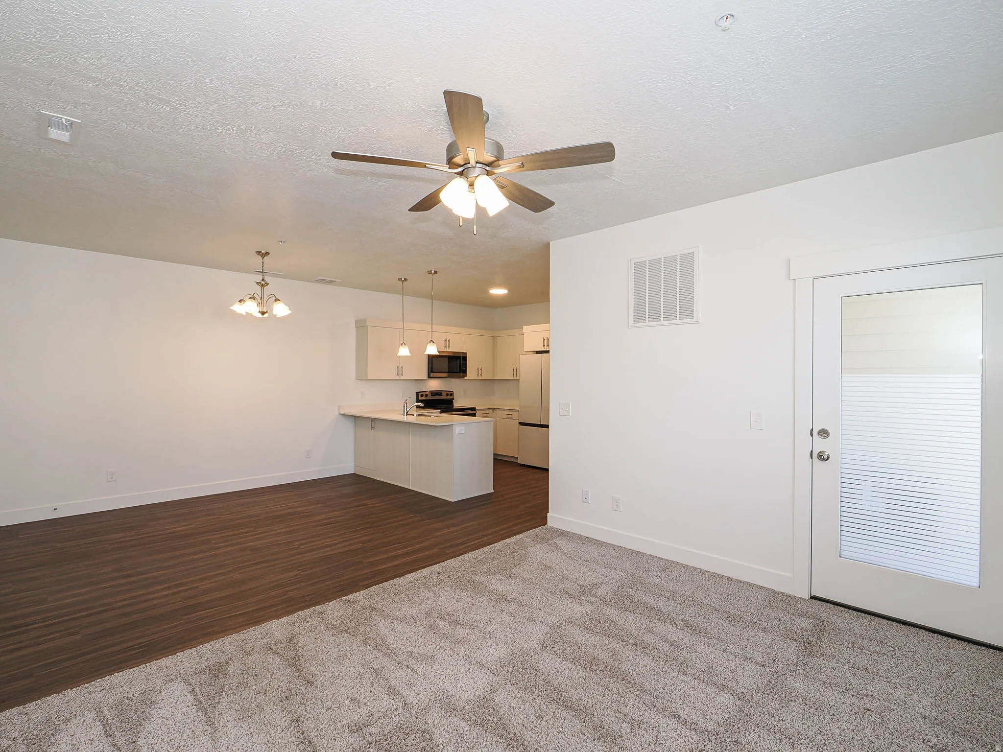 Open-concept living space with a ceiling fan, wall-to-wall carpeting, and wood-finish flooring