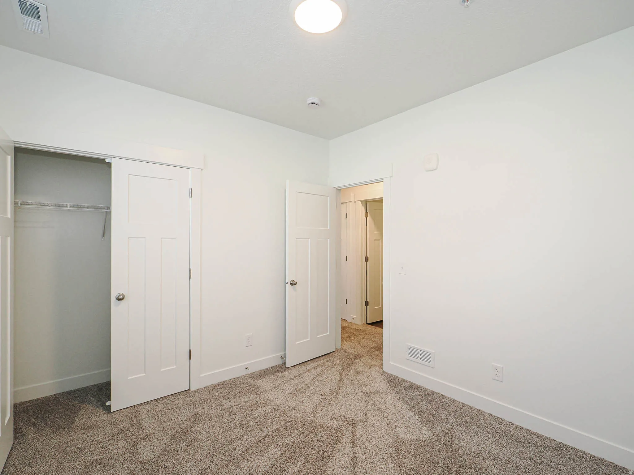 Neutral tone carpeting and white walls in a room featuring a sliding closet door, a paneled interior door, and a flush-mount ceiling light fixture