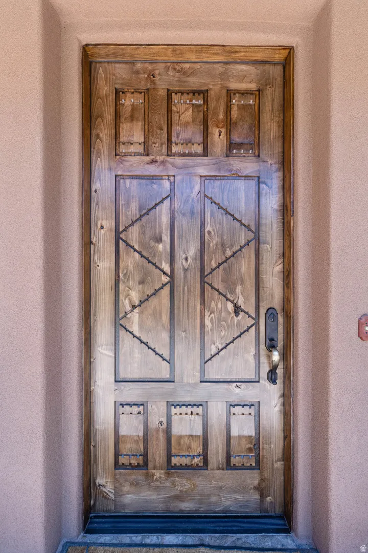 Carved wood entry door featuring decorative metalwork, a dark bronze handle, and a textured stucco surround