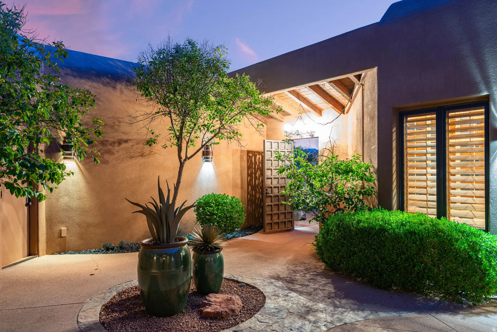 Stucco exterior featuring a covered entry, wood beam ceiling, decorative gate, and louvered window shutters