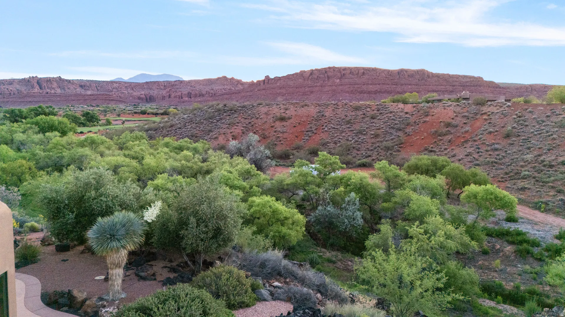 Expansive desert landscape featuring red rock formations, lush green foliage, and natural desert vegetation