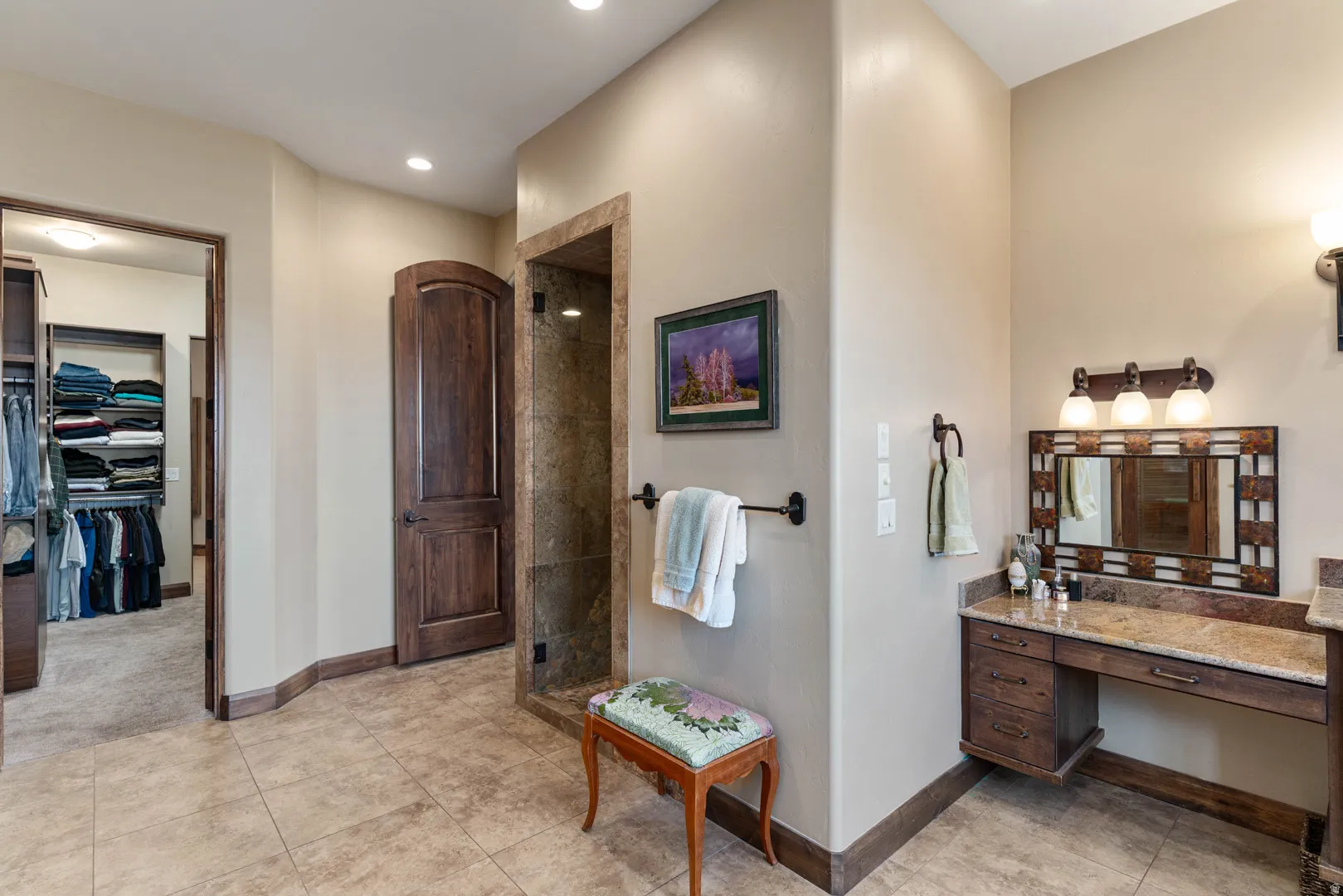Bathroom featuring tile flooring, a built-in vanity with a stone countertop, a glass-enclosed shower, and a dark wood door