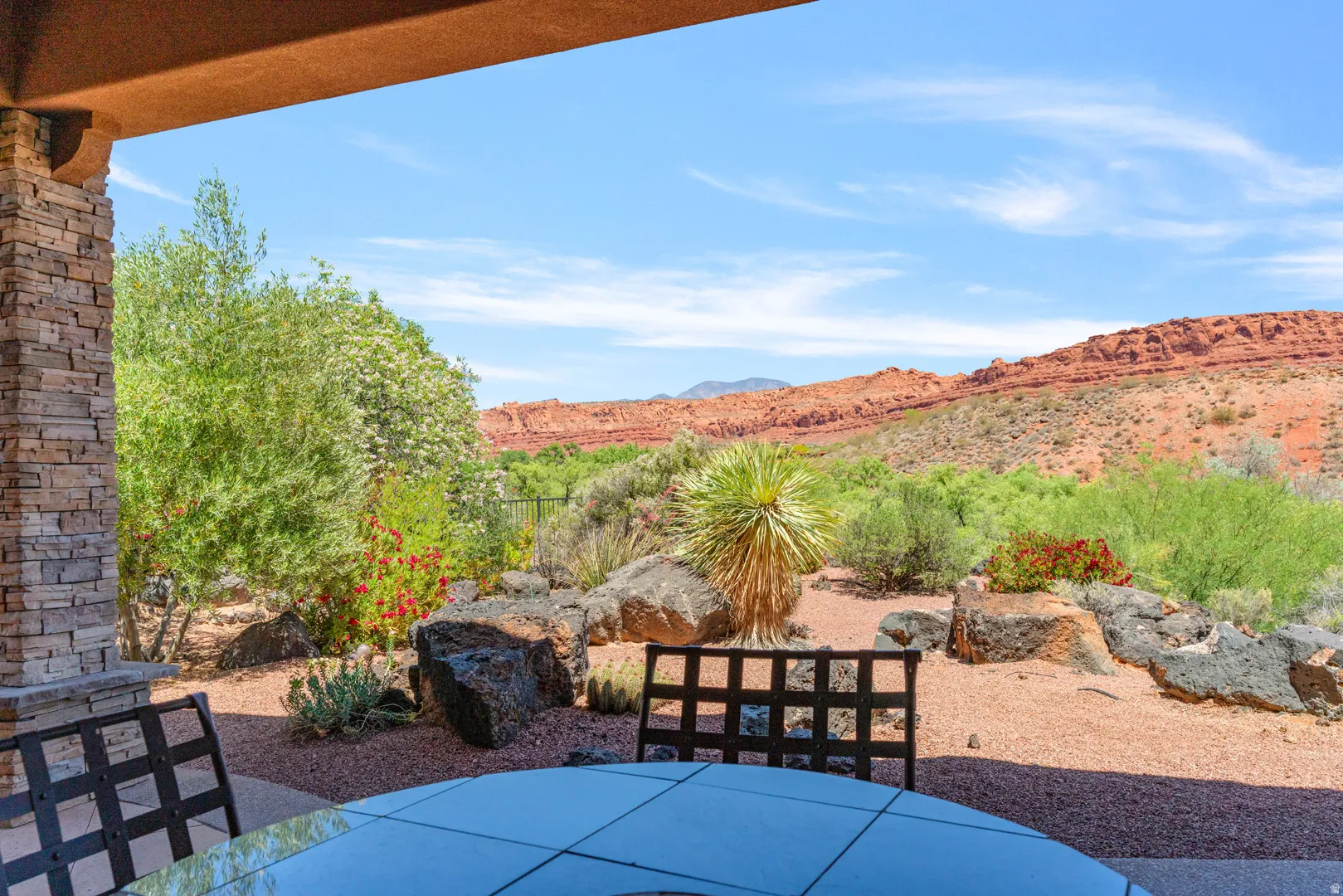 Covered patio featuring stacked stone columns, a glass-top table, and desert landscaping