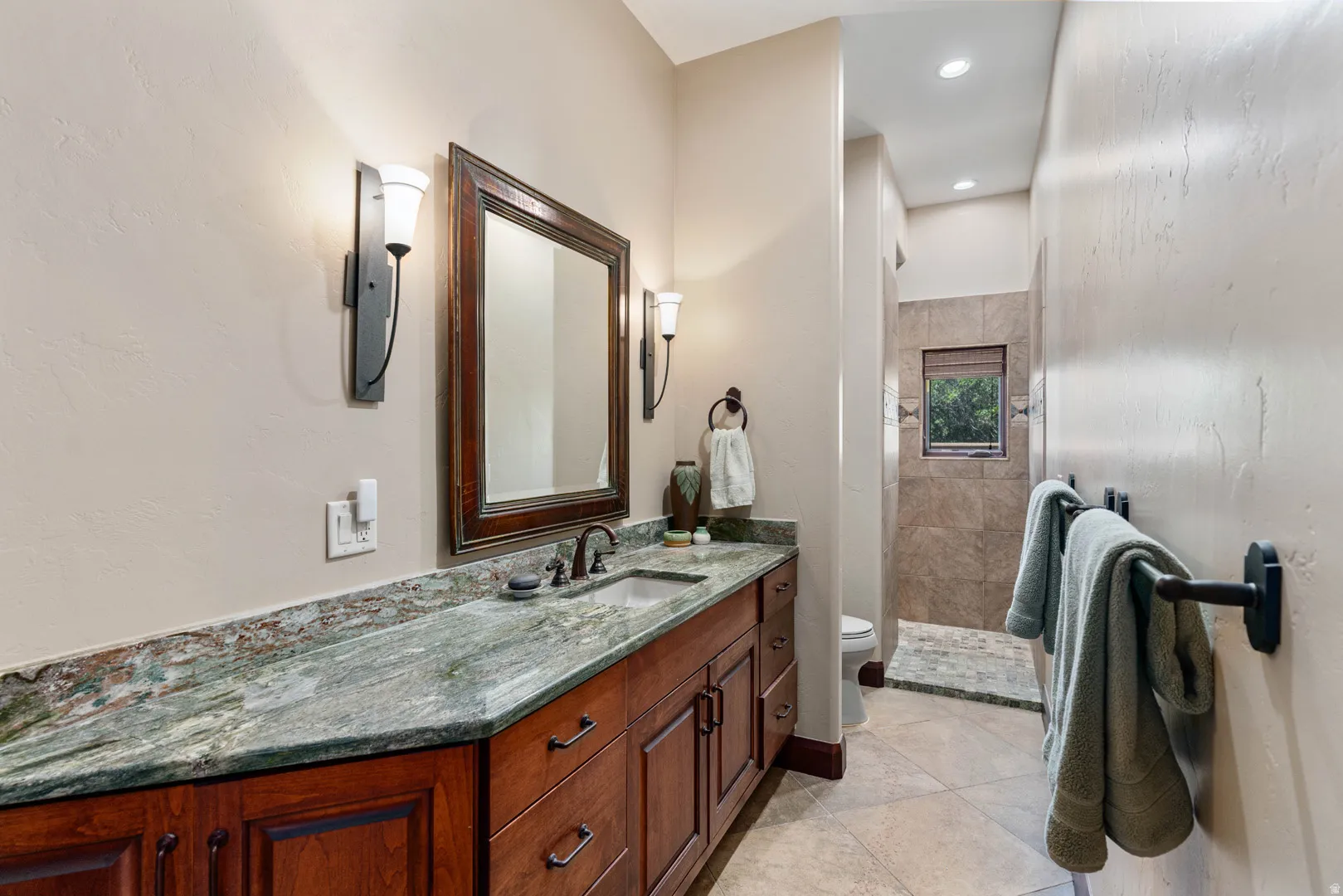 Bathroom vanity featuring a natural stone countertop, wood-finish cabinetry, and a framed mirror with sconce lighting