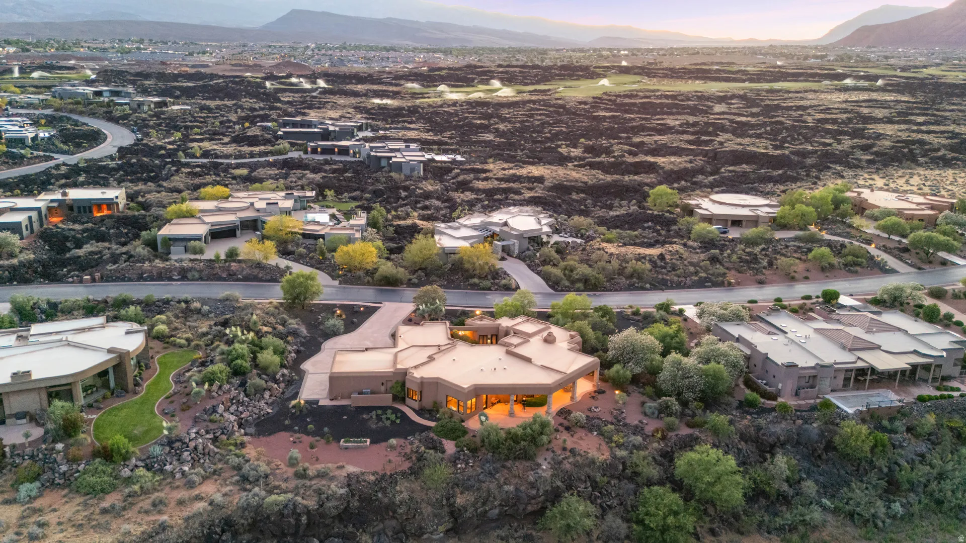 Elevated desert residence featuring a distinct architectural design, extensive paved driveway, and varied landscaping