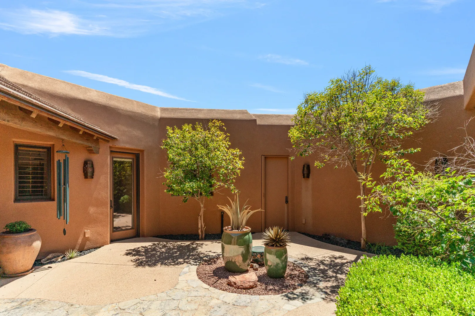 Southwestern-style exterior with a stucco finish, showcasing a flagstone and aggregate patio, mature plantings, and a solid wood entry door with glass paneling