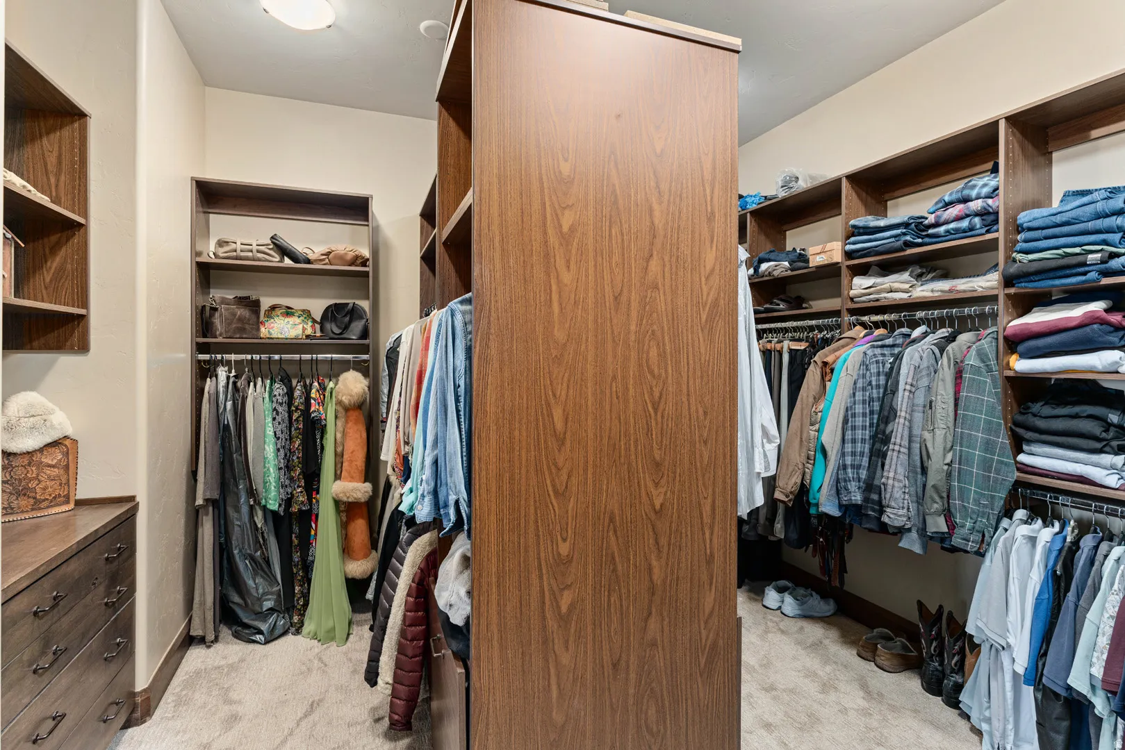 Primary custom closet system featuring wood-finish cabinetry, integrated shelving, ample hanging space, built-in dresser, and a soft carpeted floor