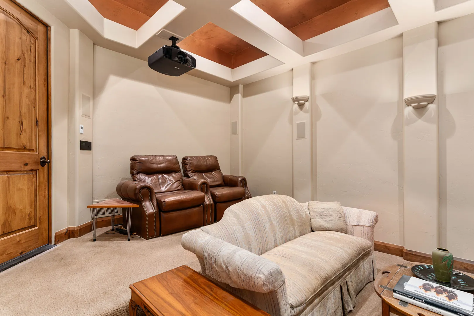 Dedicated media room featuring a ceiling-mounted projector, integrated ceiling speakers, and wall sconces