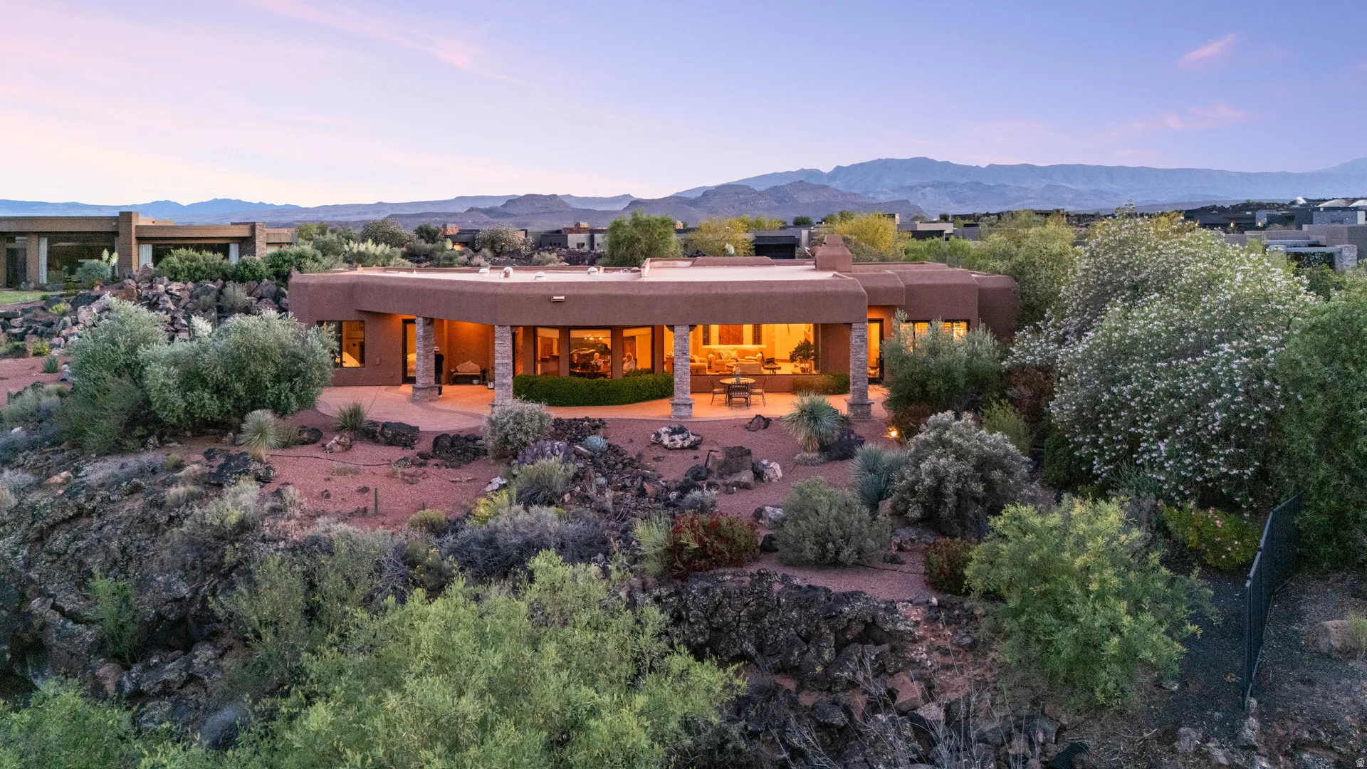Southwestern-style architecture featuring an expansive patio, natural rock landscaping, and mature desert vegetation