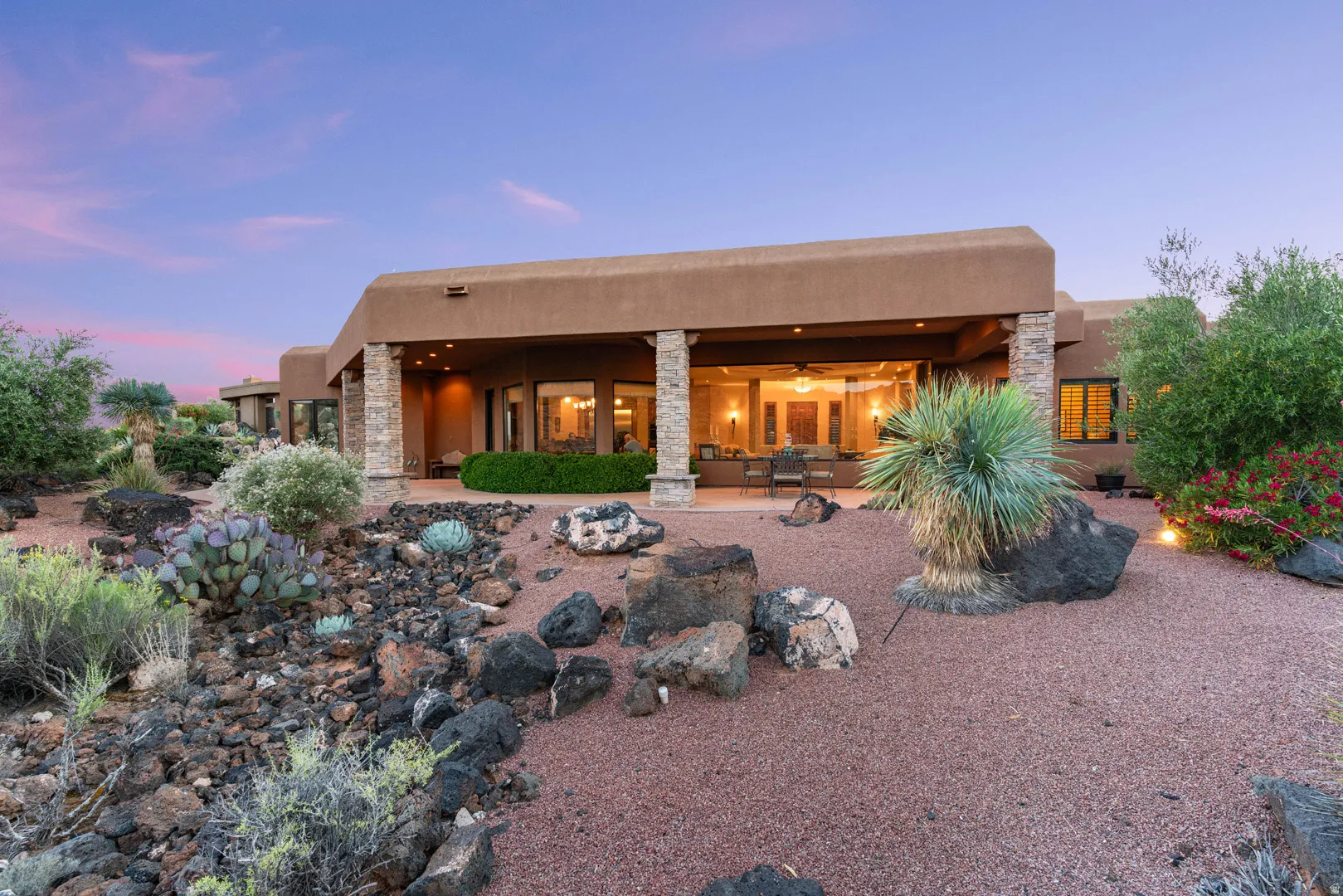 Expansive desert landscaping featuring a covered patio, stone columns, and large glass doors