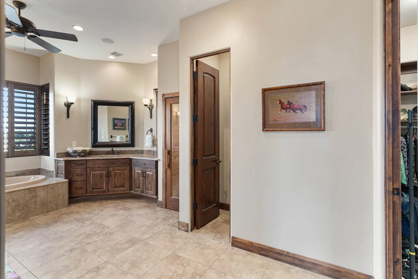Spacious bathroom featuring a corner vanity with a vessel sink, a built-in soaking tub, plantation shutters, and a ceiling fan