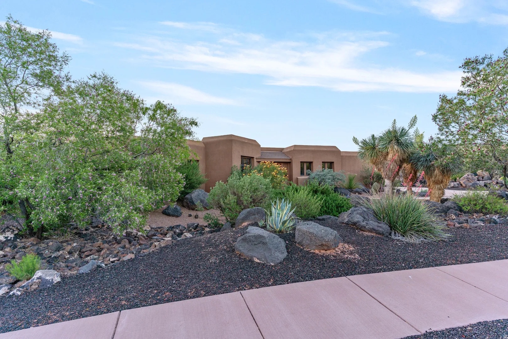 Southwestern-style stucco exterior featuring a desert landscape with mature trees and native plantings