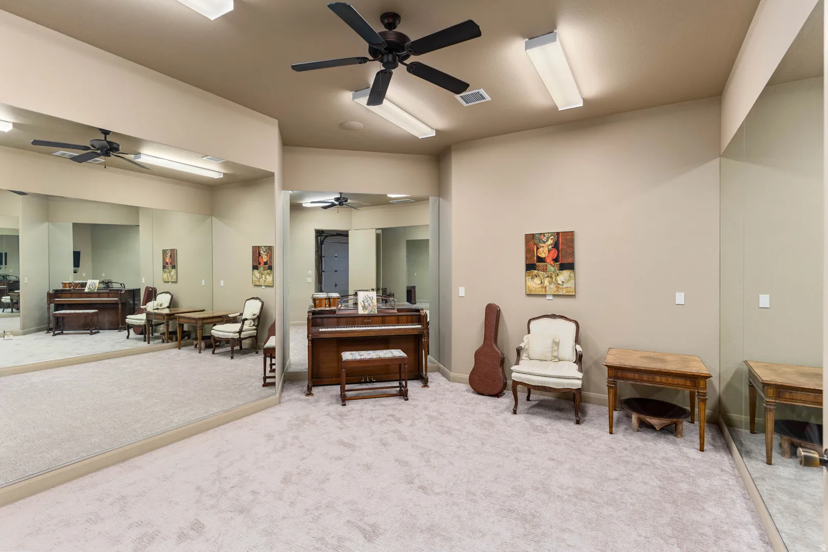 Carpeted flex room in garage featuring mirrored walls, two ceiling fans, and fluorescent lighting fixtures
