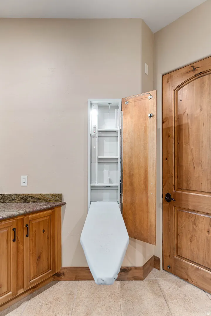 Recessed ironing board with integrated shelving, complementing the wood-finish cabinetry, granite countertop, and tiled flooring