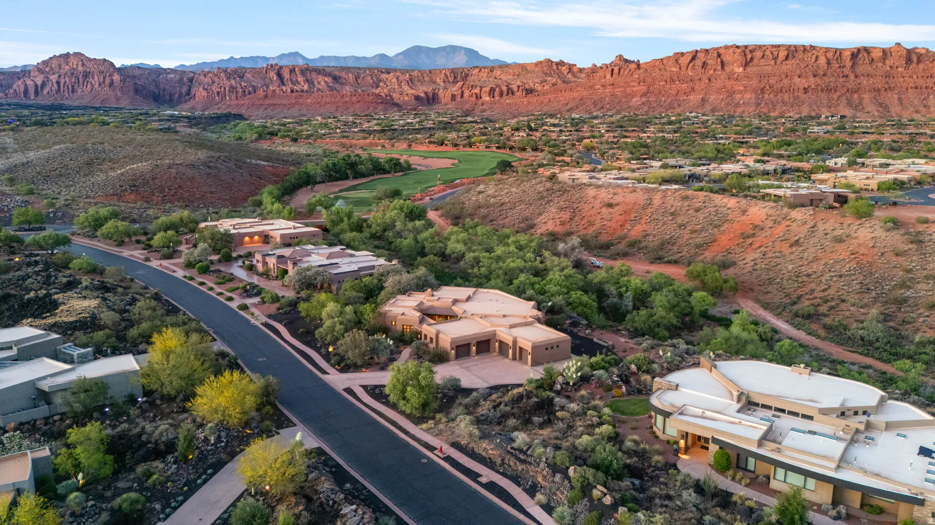 Roadway lined with modern desert architecture, surrounded by rugged red rock formations and verdant landscaping