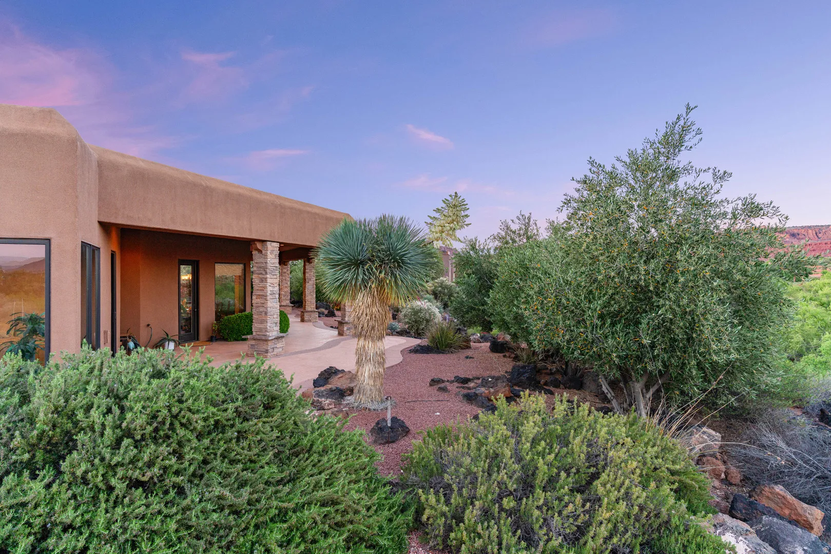 Exterior stucco siding with a covered patio featuring stone-clad pillars, large windows, and desert landscaping