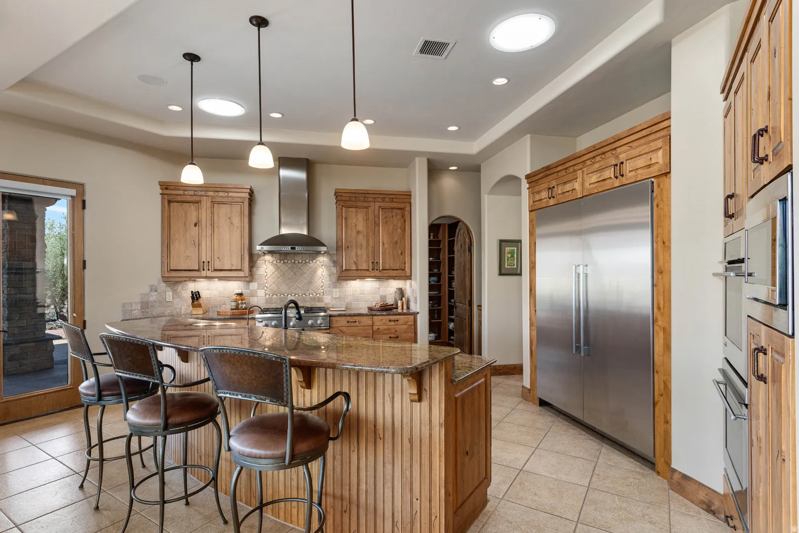 Kitchen featuring a large central island with seating, stainless steel appliances, wood-finish cabinetry, tile flooring, and recessed lighting