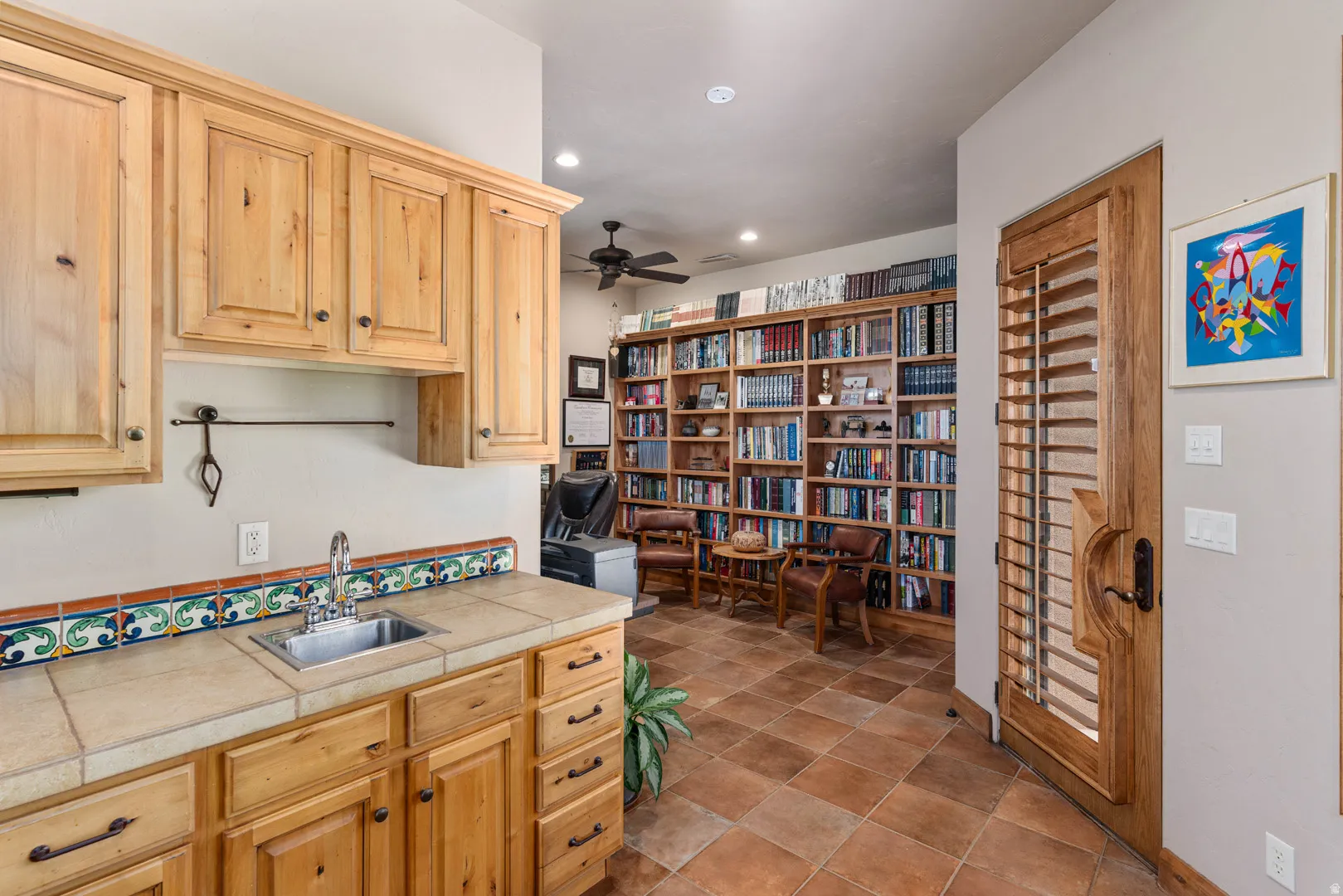 Study featuring extensive built-in shelving, terracotta-style floor tiles, and a ceiling fan