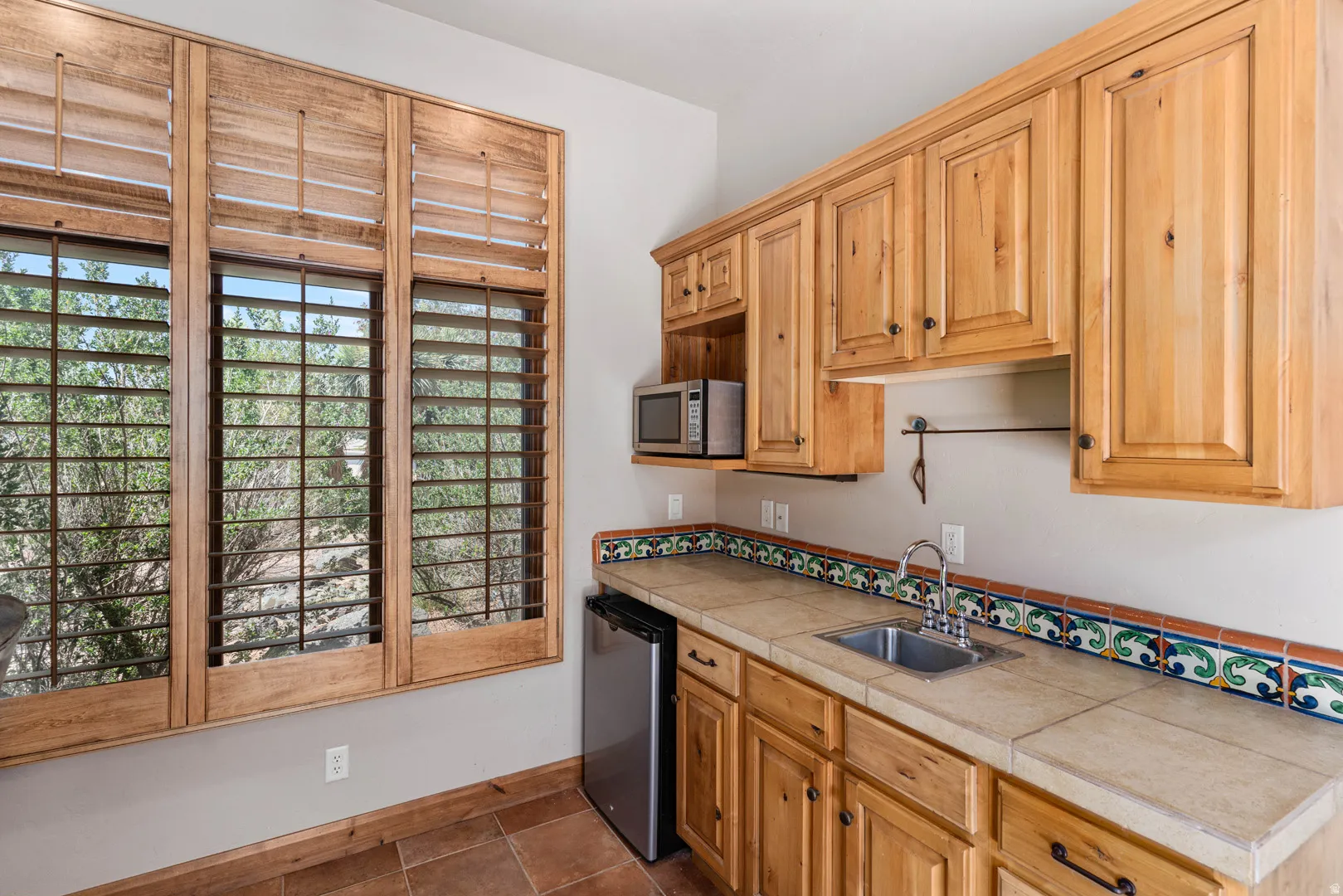 Light wood colored cabinetry and wood-finish plantation shutters complement the tile flooring