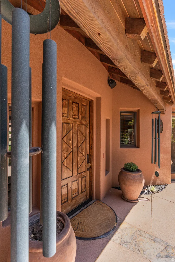 Hand-carved wood entry door with wrought iron detailing, set within an adobe-style exterior featuring visible wood beam construction and stucco finish