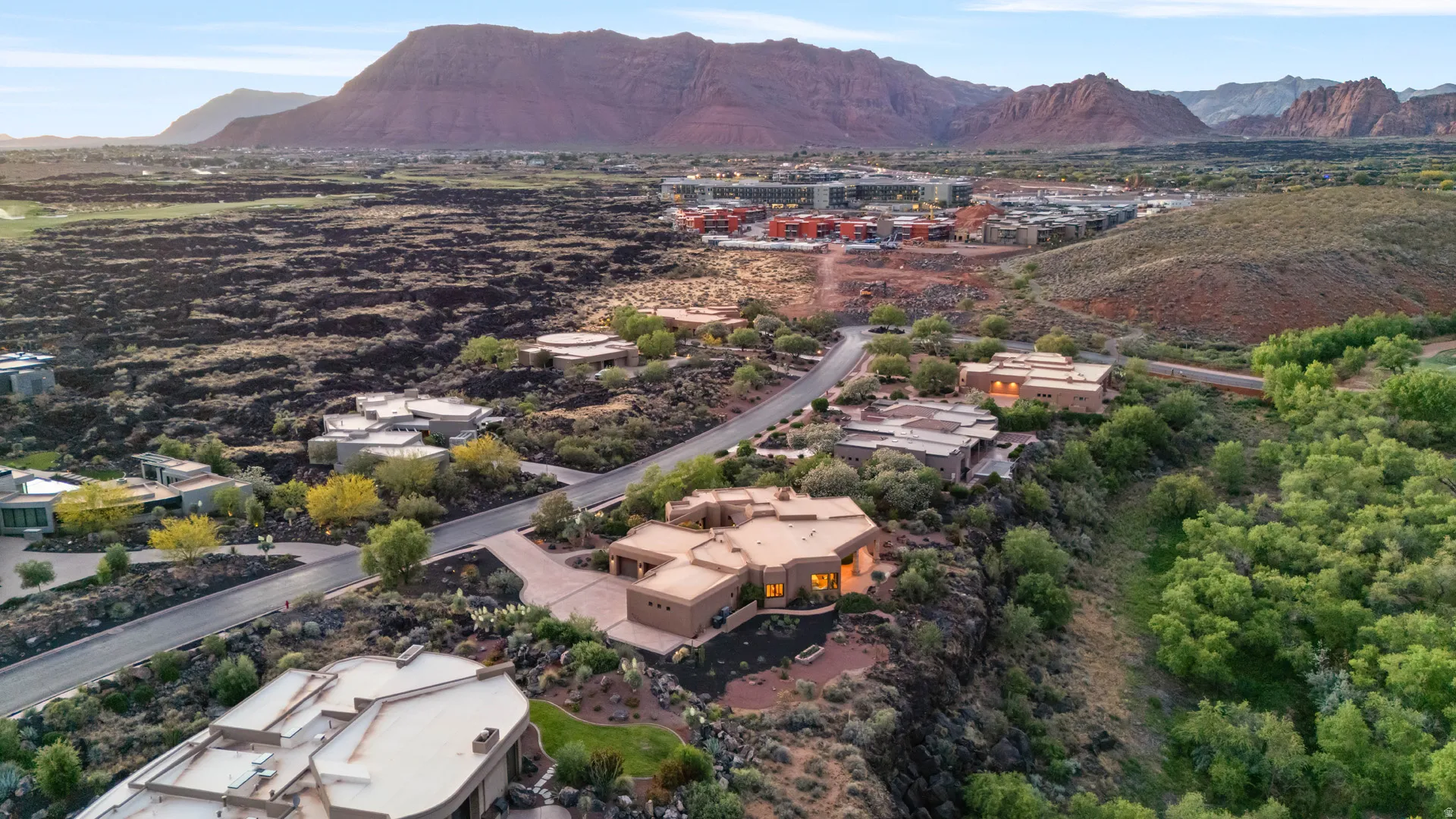 Desert landscape featuring a paved street with multiple residential structures, natural rock formations, and varied vegetation