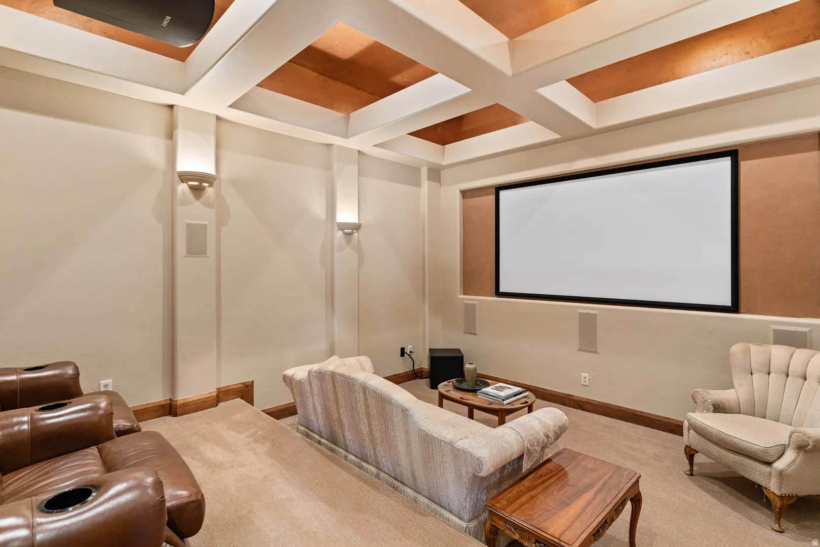 Dedicated media room featuring a large projection screen, coffered ceiling with accent panels, and built-in wall speakers