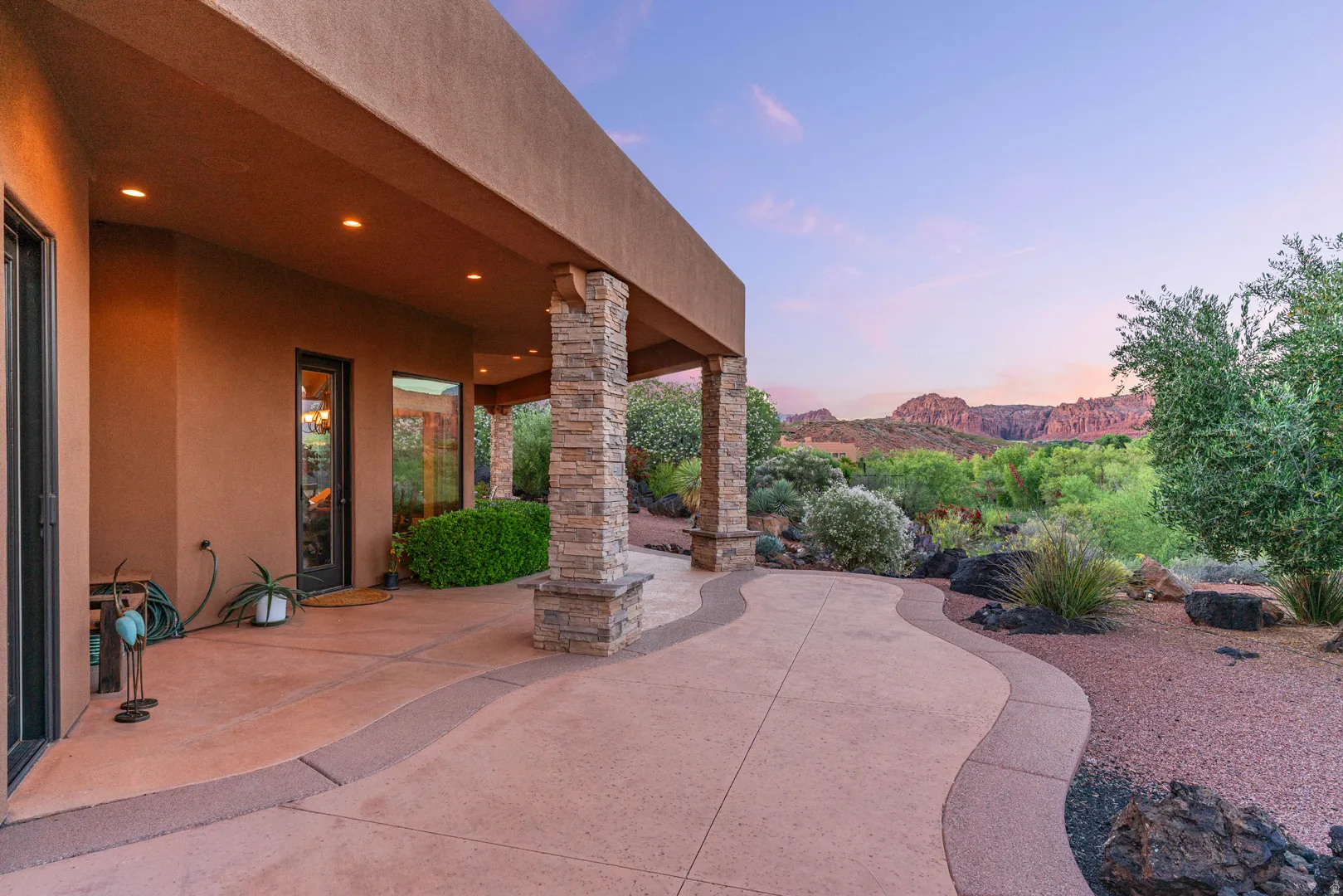 Expansive covered patio featuring integrated recessed lighting, stone-clad architectural columns, and a curvilinear concrete pathway